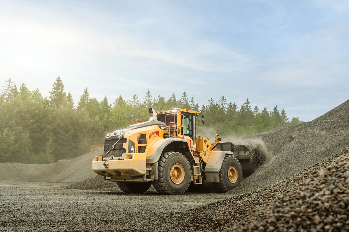 Grävmaskin som gräver grus med LBC-Ängstorps logotyp på sidan