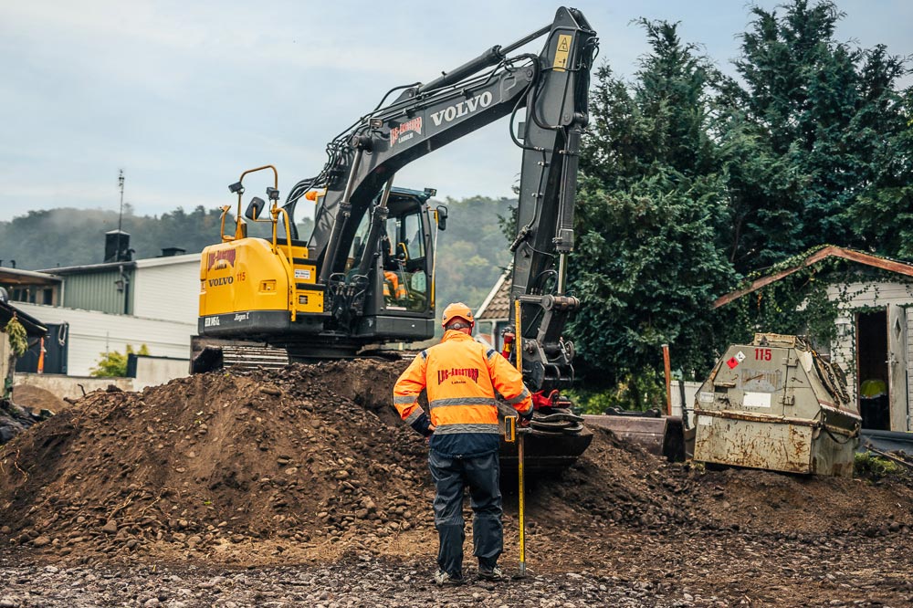 En grävskopa med en man i LBC-jacka framför på ett projekt inom entreprenad
